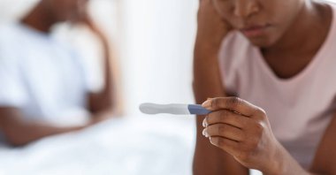 Tanımlanamayan siyah bir kadın, yatağında oturan ve pozitif hamilelik testi yapan Afro-Amerikan erkek, arka planda yatan, istenmeyen gebelik kavramı, kırpılmış, panorama. Test üzerine seçici odak