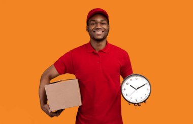 Hızlı Teslimat Servisi. Gülümseyen Afro-Amerikan Erkek Kurye Saat ve karton kutunun portresi. Kurye Çabuk Teslim Ediyor Sarı Turuncu Arkaplan 'da tek başına duruyor