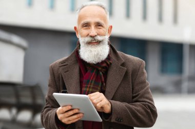 Sokakta yürürken dijital tableti tutan uzun gri sakallı, gülümseyen yaşlı adam fotokopi alanına bakıyor ve gülümsüyor. Üst düzey işadamı şık giyinmiş, evi ofis binasının yanında duruyor.