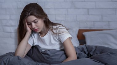 Kış depresyonu kavramı. Mevsimsel duygusal bozukluğu ya da depresyonu olan üzgün genç bir kadın yatağında yalnız oturuyor. Mutsuz kadın olumsuz düşüncelerle boğulmuş, akıl hastalığından muzdarip.