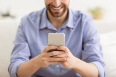 Mutlu Sakallı Adam akıllı telefon mesajları kullanıyor ve cep telefonu uygulamasını evdeki koltukta otururken kullanıyor. Harika uygulama, cep telefonu kullanan adam interneti tarıyor ya da kapalı alanda oyun oynuyor. Sığ Derinlik