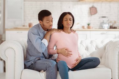 Evde doğum sancısı çeken hamile eşine destek veren endişeli siyah koca. Güzel Afrikalı Amerikalı kadın acıdan muzdarip, partnerinin yardımıyla doğum yapıyor.