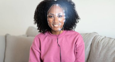 Yüz tanıma sistemi kimlik taraması yaparken kıvırcık saçlı Afro-Amerikalı kadın gülümsüyor. Bu teknoloji, çeşitli ortamlardaki günlük etkileşimimizin merkezi haline geliyor..