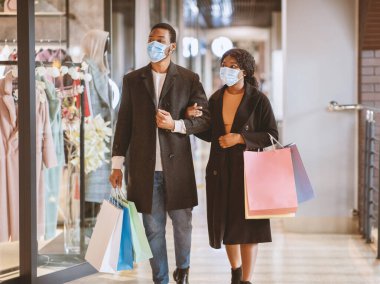 Bir çift dükkan penceresinin önünden geçip içeri bakıyor. Bin yıllık Afro-Amerikan erkek ve kadın koruyucu maskeler takıp alışveriş merkezinde alışveriş yapıyor ve Kara Cuma 'da covid-19 salgını sürüyor.