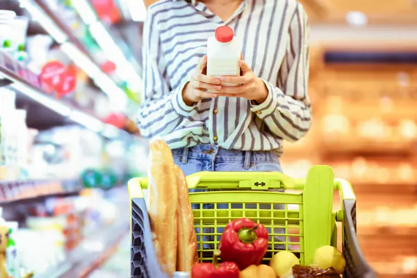 Market alışverişi. Tanımlanamayan bir kadın müşterinin elinde süt ya da yoğurt şişesi var ve yiyecek dolu bir yük arabasına koyuyor. Alışveriş merkezinde sağlıklı süt ürünleri alan genç bir kadın.
