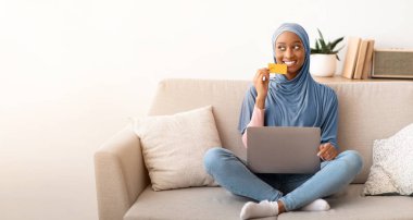 Kanepede dizüstü bilgisayarı ve kredi kartıyla oturan neşeli Afro-Amerikan bayan evde internetten alışveriş yapıyor, fotokopi çekiyor. Başörtüsü takmış gülümseyen siyah kadın, kapalı mekanlardan mal alıyor.