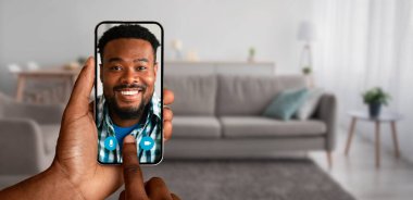 Bir insan evinden yapılan bir video görüşmesinden zevk alıyor, akıllı telefonunun ekranında gülümseyen adamla bağlantı kuruyor, modern iletişimin kolaylığını gösteriyor..