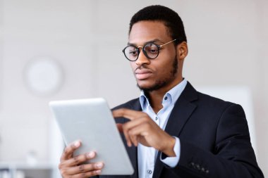 Modern dijital tablet kullanarak ciddi siyahi girişimcilere yakın çekim, online ticaret ve stokları kontrol, ofis içi, kopyalama alanı. Genç Afrikalı Amerikalı yönetici dijital ped tutuyor.