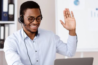 Ofis çalışanı konsepti. Kulaklığı laptop ekranında, ofis içinde, boş alanda sallanan mutlu Afrikalı Amerikalı adam danışmanı. Çevrimiçi çalışan, gözlük takan neşeli siyahi işveren.