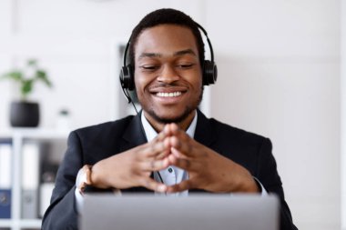 Kulaklıklı siyahi iş adamının bilgisayarı kullanması, müşteriyle ya da iş ortağıyla neşeli bir şekilde konuşması, bilgisayar ekranına gülümsemesi, Afro-Amerikalı adamın iş eğitimi alması, kopyalama alanı.