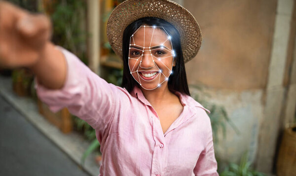 Человек занимается инновационной технологией распознавания лиц на открытом воздухе. Человек улыбается, демонстрируя цифровое наложение, подчеркивающее черты лица в яркой городской обстановке.