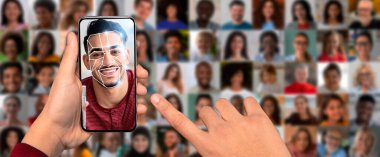 Bir kişi elinde yüz tanıma teknolojisini gösteren bir akıllı telefon tutuyor. Cihaz, arka planda çeşitli yüzler kolajıyla çevrili, dijital bir kaplamayla gülümseyen bir yüz sergiliyor.