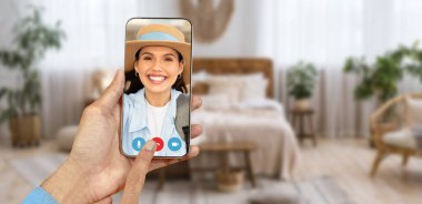 Bir insan rahat oturma odasından gelen bir video görüşmesine katılmak için akıllı telefon kullanıyor. Ekranda gülümseyen bir yüz var, evden online iletişimin bağlantısını vurguluyor.