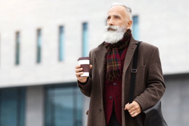 Sıcak kıyafetler içinde yakışıklı yaşlı bir adam ofise gidiyor, kahve içiyor, deri çanta taşıyor, fotokopi odasına bakıyor. Yaşlı gri saçlı adam caddede yürüyor, kahvesini içiyor, iş merkezi arkada.