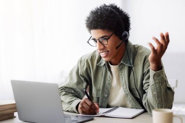 Çevrimiçi iletişim ve web tabanlı öğrenme. Memleketinden laptopuyla üniversite hocasıyla konuşan pozitif siyah bir genç. Yakışıklı Afrikalı Amerikalı öğrenci webcam 'de video görüşmesi yapıyor.