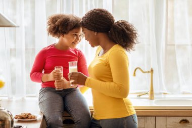 Siyah aile annesini ve kızını sevmek, mutfakta abur cubur yerken, ev yapımı kurabiye yerken, birlikte süt içerken, Afrikalı bir annenin mutlu çocuğuyla alınlarına dokunması,