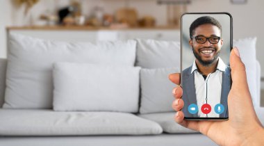 Bir insan oturma odasından canlı bir video izlemekten zevk alır, ekranda gülümseyen bir şahsın olduğu bir akıllı telefon tutar. Samimi ortam iletişim deneyimini geliştirir..