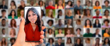 Bir insan yüzüne akıllı telefon dayayıp yüz tanıma teknolojisini çalıştırıyor. Arkalarında çeşitli yüzlerden oluşan bir kolaj var, modern tanımlama yöntemlerini eylem halinde sergiliyorlar..