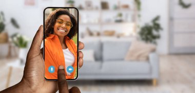 Bir insan akıllı telefonuyla iletişim kurar, evinden bir video görüşmesi yapar. Arka planda rahat bir yaşam alanı var. Sohbetin rahat atmosferini arttırıyor..