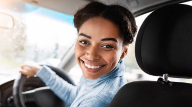 Sürücü yolcu koltuğuna döner ve kameraya gülümser. Bin yıllık Afro-Amerikan kadın taksi şoförü direksiyonda oturuyor, akıllı telefonun yanında boş ekranlı, panorama