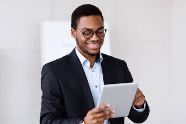 Pozitif siyahi genç girişimci ofiste dijital tablet kullanıyor, boşluğu kopyalıyor. Gülümseyen Afrikalı Amerikalı yönetici ajandasını kontrol ediyor, modern iş teknolojilerinin tadını çıkarıyor.