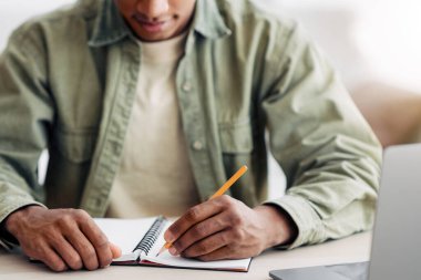 Uzaktan öğrenme konsepti. Evdeki online ders sırasında not defterine yazan siyahi öğrenci, ellerine odaklan. Webinar 'a katılan, eğitim kursuna katılan Afrikalı Amerikalı gençlere bakış açısı
