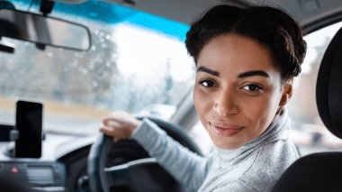 Kadın sürücü arka koltukta ya da otomobil blogunda yolcuyla konuşuyor. Neşeli, çekici, Afro-Amerikalı bir kadın direksiyon tutuyor, kamerada omzunun üzerinden bakıyor, boş bir alan.