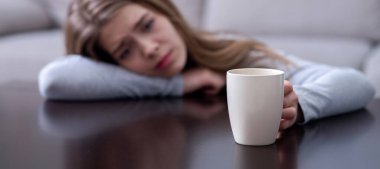 Masaya yaslanmış ve elinde sıcak içecekle depresyon geçiren melankolik genç bir kadın. Seçici odaklanma. Uzayı kopyala Ruh hali değişimleri ya da psikolojik sorunlar kavramı