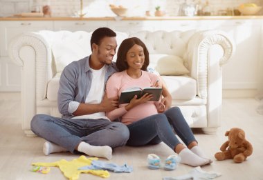 Bekleyen neşeli çift oturma odasındaki doğum hastanesi için bebek eşyaları listesi yazıyor. Mutlu anne ve babalar doğum merkezine hazırlık yapıyor, deftere not tutuyorlar.