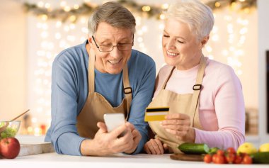 Yaşlı bir çift cep telefonu ve kredi kartı kullanıyor internetten alışveriş yapıyor ve Noel 'de evde mutfaktaki restoranda yemek siparişi veriyor. Mobil Bankacılık Uygulaması