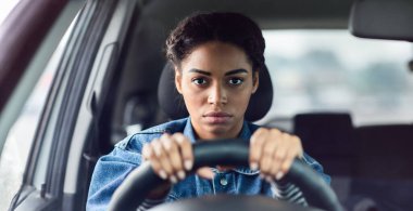 Yüz ifadesi, olumsuzluk, stres ve trafik sıkışıklığı. Ciddi şekilde üzgün genç Afrikalı Amerikalı bir bayan direksiyonun arkasında oturuyor ve pencereye doğru gergin bir şekilde bakıyor.