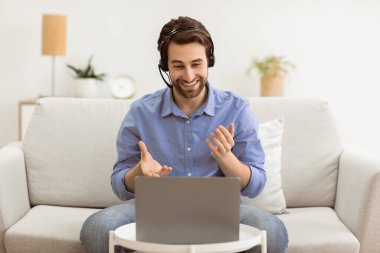 İş adamı Laptop 'ta Eğitimci İşletmeleri izlerken çevrimiçi olarak koltukta oturan kulaklığı takıyor. Uzak Bilgisayar Çalışmaları, Video Çağrısı ve İnternet İş Eğitimi Konsepti