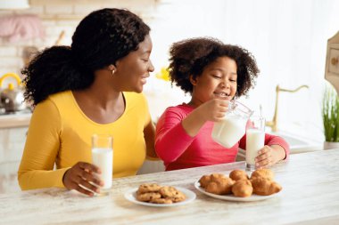 Siyah anne ve kızı süt içiyor ve mutfakta ev yapımı hamur işlerinin tadını çıkarıyor, birlikte çerez yiyor ve evde eğleniyorlar. Sağlıklı Kalsiyum Bardağa İçen Şirin Küçük Kız, Yakın plan