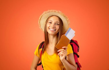 Sırt çantasında pasaport ve uçuş biletleri olan sırıtan genç bir turist. Stüdyo sarı. Neşeli bayan gezmeye hazır, kameraya bakıyor ve gülümsüyor, boşluğu kopyalıyor.