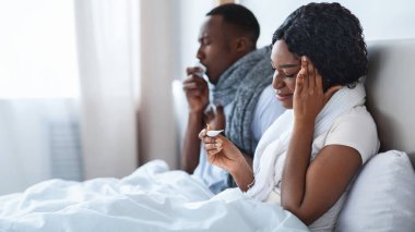 Yatak odasında eşarba sarılmış hasta siyah bir çift, ateşi ölçüyor ve burunları aksıyor. İki kişilik genç Afrikalı aile hastalandı, evde kaldılar, mevsimlik virüsler ve grip konsepti