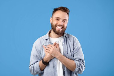 Milenyum adamı elini göğsüne dayayıp mavi stüdyo arka planında olumlu duygular ve minnettarlığını ifade ediyor. Mutlu genç adam avucunu kalbinde tutuyor, umut ve aşkı hissediyor.