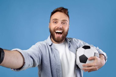 Mobil cihazdan özçekim alan toplu mutlu futbol fanatiği mavi stüdyo arka planında. Maçtan sonra en sevdiği takımı için tezahürat yapan pozitif bir futbolcu.