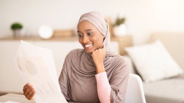 Uzaktan çalışma konsepti. İçeride dizüstü bilgisayarın yanında çalışan tesettürlü siyahi kadın. Arap türbanlı Afrikalı Amerikalı kadın iş raporu yazıyor.