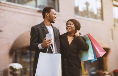 Akıllı telefon kullanan heyecanlı arkadaşlar Kara Cuma 'da internetten alışveriş yapıyor ve mutlu olduklarını ifade ediyorlar. Milenyum Afrikalı, siyah çantalı ve akıllı telefonlu Amerikalı karı-koca alışveriş merkezinden çıkıyor.