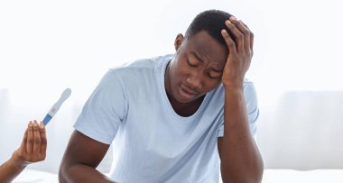 İstenmeyen hamilelik ve ilişkiler. Hamile olan kızgın siyah kadın şok olmuş erkek arkadaşına bağırıyor. Kafasına dokunuyor. Afro-Amerikan çift evde yatakta oturuyor.