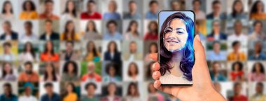 Bir insan yüzünün yüz taramasını gösteren bir akıllı telefon tutar. Arkalarında, modern kimlik teknolojisini harekete geçiren çeşitli bir kalabalık görülüyor..