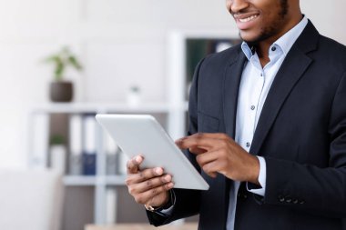 Gülümseyen siyah yönetici dijital tablet, ofis içi, fotokopi alanı kullanıyor. Mutlu Afro-Amerikan iş adamı iş uygulamasını kullanıyor, kullanıcı dostu yazılımın keyfini çıkarıyor.