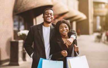 Kara Cuma günü alışveriş merkezinde yürüdükten sonra alışveriş kolikleri ve tatilden önce sezonluk indirimler. Mutlu Afro-Amerikan karı ve koca paltolarını giyer, bir sürü renkli çanta taşır ve sarılırlar, açık havada, kopyalama alanı