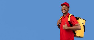 En İyi Teslimat Hizmeti Konsepti. Kırmızı üniformalı ve termal çantalı özgüvenli gülümseyen siyah kurye portresi baş parmak işareti yapıyor ve mavi arka planda izole edilmiş kameraya bakıyor.