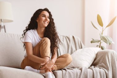 Evdeki kanepede oturan neşeli genç bayan fotokopi odasına bakıyor ve gülümsüyor. Güzel kıvırcık kadın rahat oturma odasında dinleniyor, boş bir yere bakıyor, haftasonunu yalnız geçiriyor.