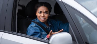 Çatışmalar, zorluklar ve şehir yolunda sorunlar. Heyecanlı, kızgın, Afro-Amerikan kadın sürücü elinde direksiyon, kameraya bakıyor ve camdan dışarı bakıyor ve arabada, yan görüşte küfrediyor.