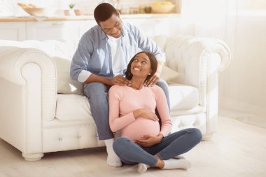 Evdeki hamile karısına masaj yapan yakışıklı siyahi adamın tam boy portresi. Afrikalı Amerikalı bir adamı sevmek, kız arkadaşının omuzlarına masaj yapmak, gelecekteki annesiyle ilgilenmek...