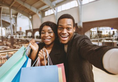 Modern şehir alışveriş merkezlerinde alışveriş torbalarıyla ahlâksız randevular. Genç, gülümseyen Afro-Amerikan erkek ve kadın portresi. Hafta sonu indirimde konuşuyorlar ve Kara Cuma 'da selfie çekiyorlar.