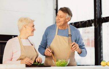 Olumlu kıdemli çift yemek pişiriyor, birbirlerine gülümsüyor, modern mutfaklarında duruyorlar. Yaşlı Eşler Sağlıklı Salata Hazırlamak İçin Yemek Hazırlıyor. Sağlıklı Beslenme