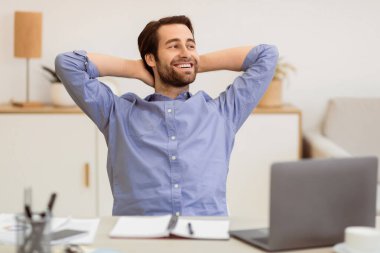 Başarılı bir iş kariyeri. Modern ofisteki iş yerinde dizüstü bilgisayarın başında oturan ve hayatından ve işinden memnun olan rahat bir adam. Tasasız İşadamı Kavramı